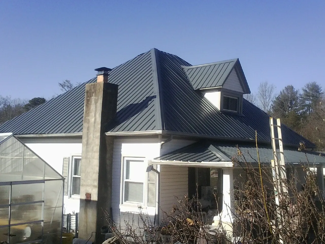 Dark blue standing seam metal roof on a white farmhouse with dormer — Slate & Tile Roof Repair by Roofing Brothers in Mongo