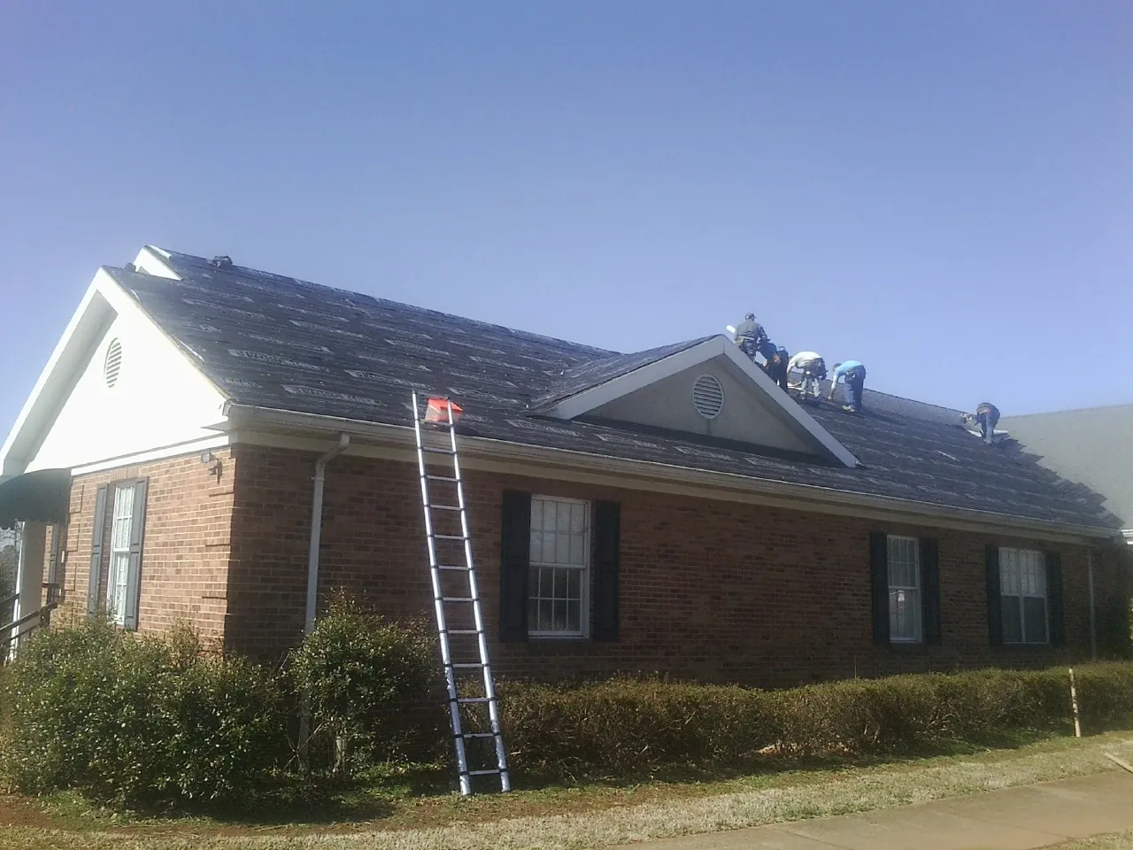 Crew tearing shingles off a brick ranch roof with a ladder set — Emergency Roof Repair work by our crew in Mongo