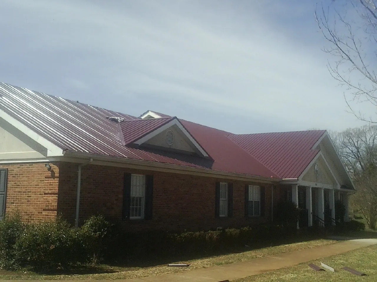 Red metal roof with gabled entries on a long brick building, from a Hail Damage Roof Repair job in Mongo