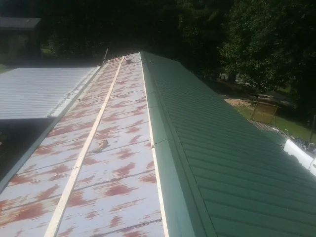 Old rusted panels beside newly installed green metal roofing — Wind Damage Roof Repair by Roofing Brothers in Mongo