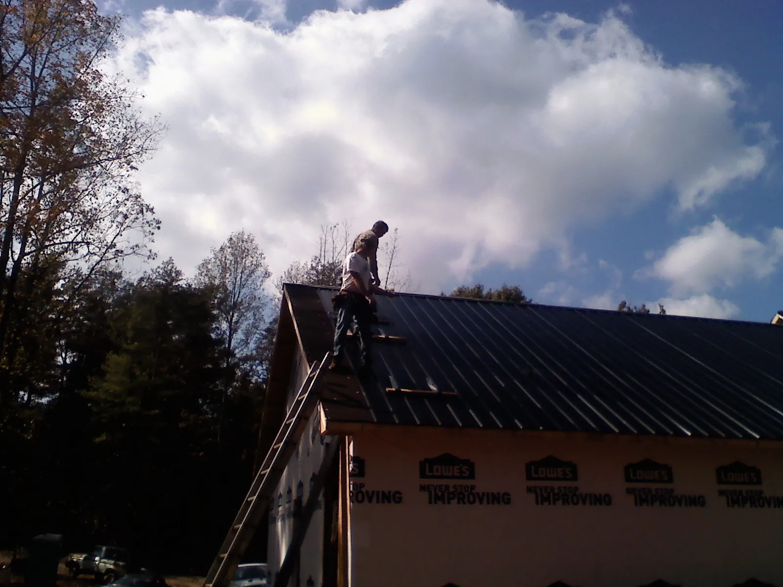 Roofer fastening dark metal panels high against a cloudy sky, from a Roof Inspection job in Mongo