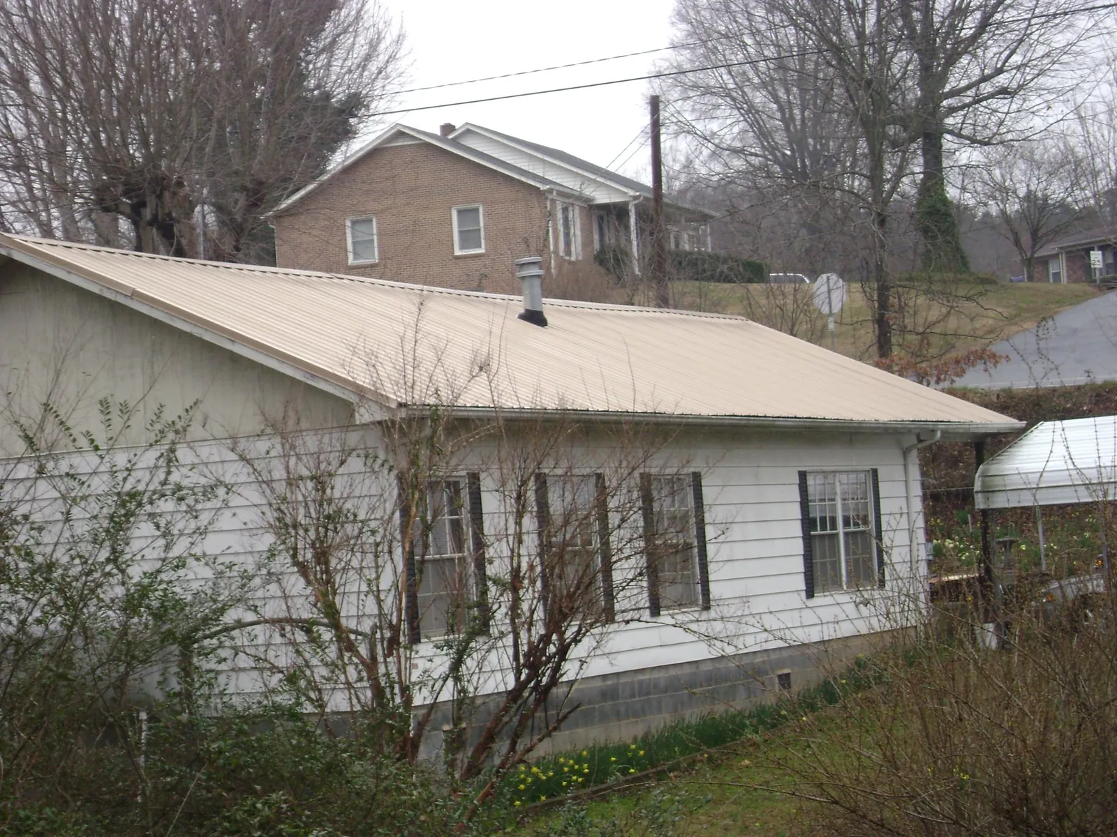 Tan metal roof on a white sided house set into a hillside — Commercial Roofing by Roofing Brothers in Mongo